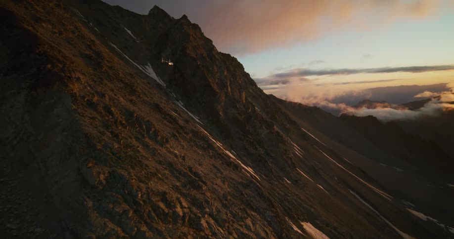 A helicopter skillfully navigates through a natural rock arch on a majestic, snowy mountain during a stunning golden hour sunset