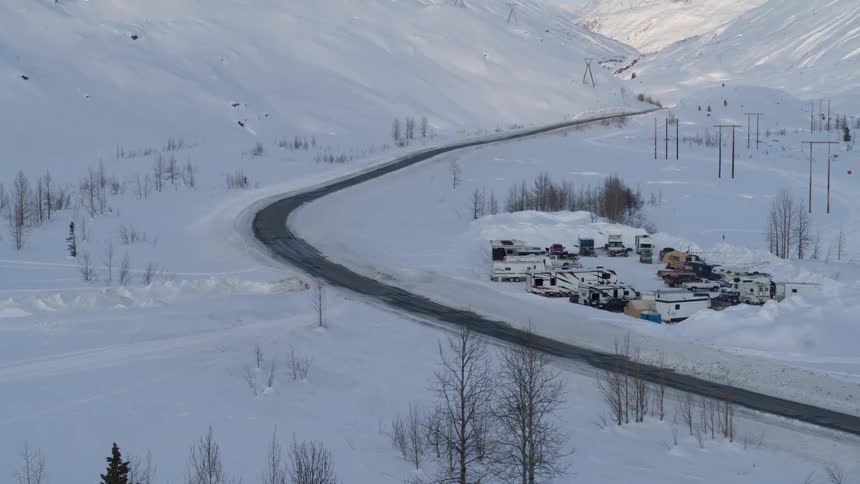 Time-lapse footage shows shadows moving across a snowy mountain pass with an RV camp set up in a valley
