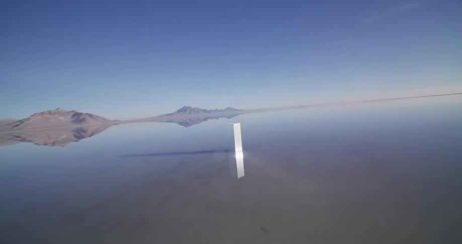 A mysterious metal monolith stands alone in the vast, reflective waters of the Bonneville Salt Flats, creating a surreal and otherworldly landscape