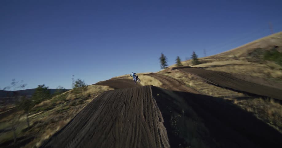 A motocross rider soars through the air in slow motion after launching off a large dirt jump on a sunny day