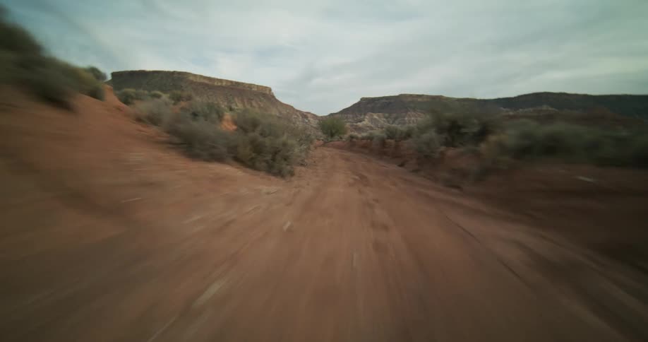 A thrilling first-person view of a high-speed drive down a winding dirt road through a remote desert canyon landscape