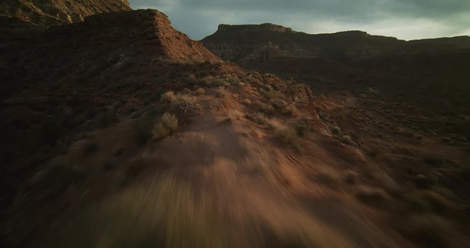 A fast-paced FPV drone flight soars over a rugged desert mountain ridge as the sun rises over the horizon