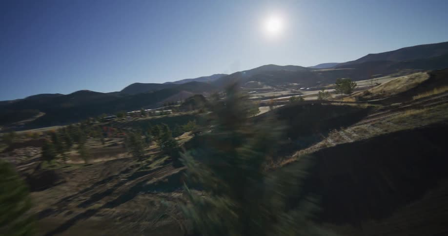 Dynamic FPV drone shot follows a motocross rider speeding along a winding dirt track in the sunny, rural mountains