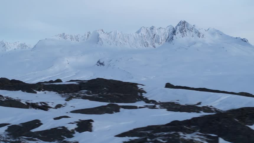 A breathtaking aerial dolly shot slowly reveals the vast, desolate beauty of a snow-covered mountain range