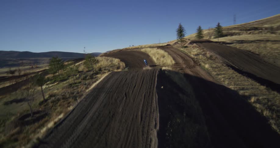 Dynamic follow shot of a motocross rider launching off a large dirt jump and soaring through the air on a hilly rural track
