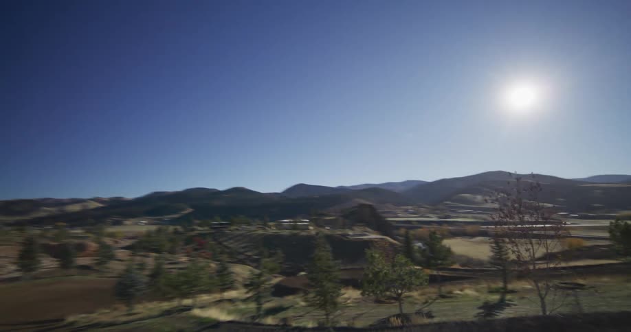 A motocross rider soars through the air in slow motion off a dirt jump, with the camera following to reveal a scenic mountain valley below