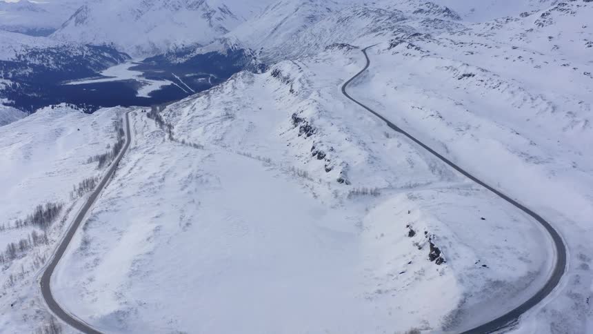 A breathtaking aerial view follows a remote road winding through a vast and snowy mountain landscape