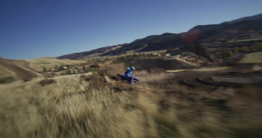 A professional motocross racer drifts around a corner on a dirt track in slow motion, kicking up a cloud of dust