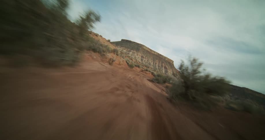A thrilling first-person view of driving fast down a winding dirt road in a rugged desert canyon under a cloudy sky