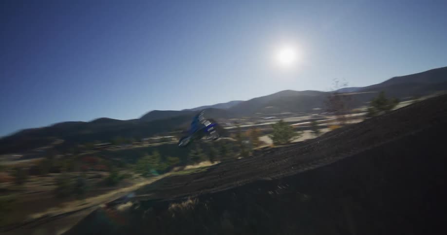 Dramatic slow-motion tracking shot of a motocross rider launching off a jump on a professional dirt track in the mountains