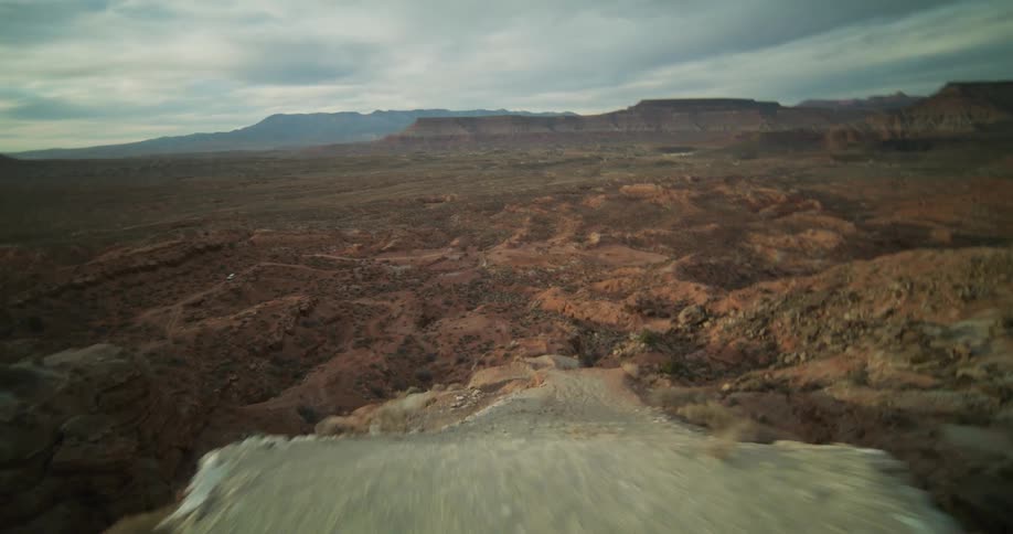 Dynamic FPV drone footage captures a thrilling flight along a rocky ridge before diving into the vast desert canyon below