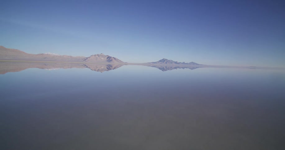 The still waters of the Bonneville Salt Flats create a surreal mirror reflection of the distant mountains under a vast blue sky