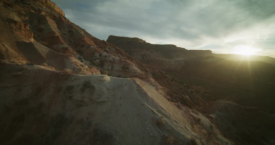 An epic aerial reveal shot flies up a rocky desert mountain to show a vast canyon valley as the sun sets