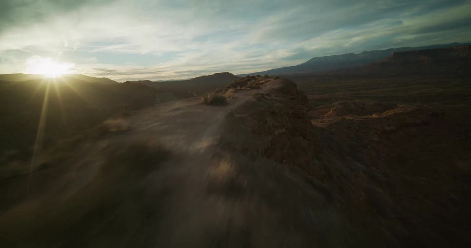 A thrilling first-person aerial flight soars along a rocky desert ridgeline into the golden sunset