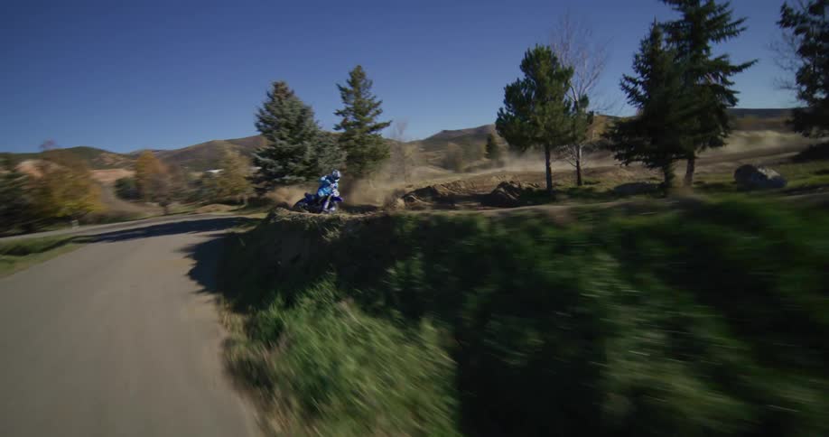 A motocross rider in slow motion kicks up a large cloud of dust while making a sharp turn on a dirt track