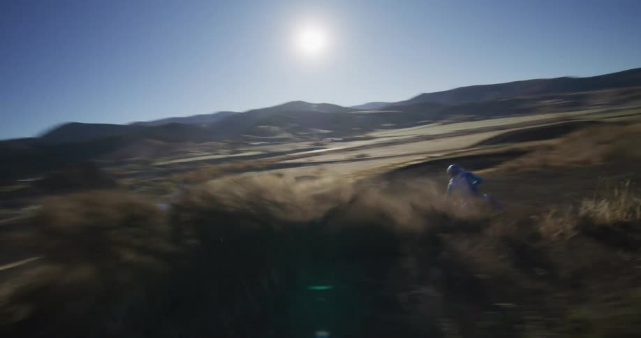 A motocross rider expertly handles a sharp turn, kicking up a cloud of dust on a sunny hillside track