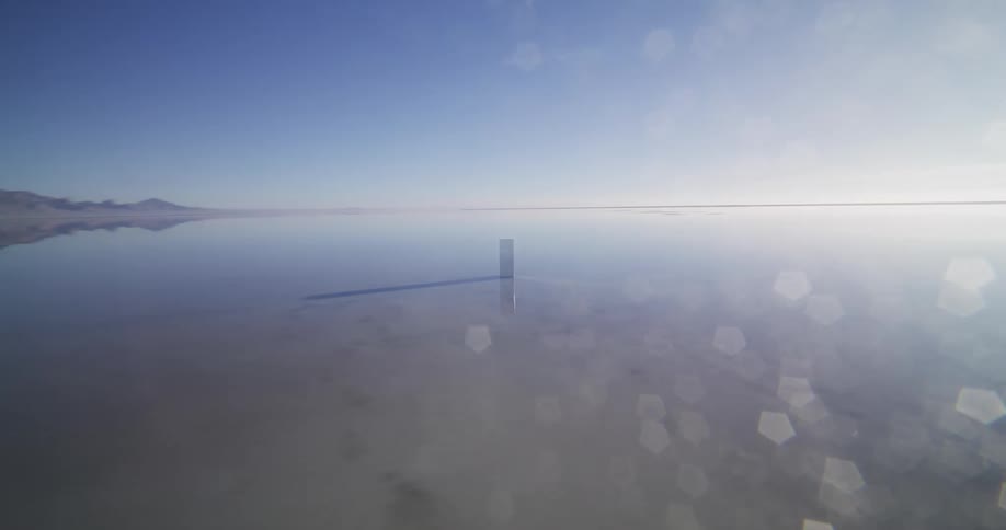 A mysterious monolith stands alone in the vast, reflective waters of the Bonneville Salt Flats, creating a surreal and otherworldly scene