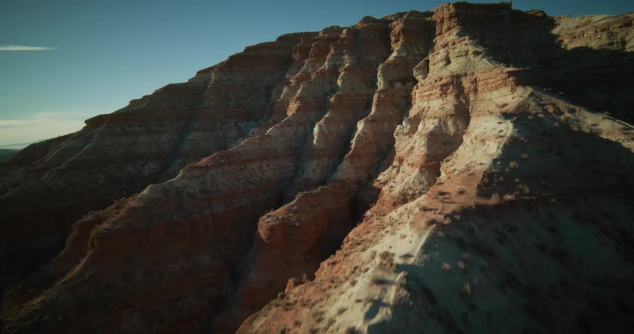 A slow aerial pass reveals the intricate textures and warm colors of a layered red rock canyon wall at sunrise
