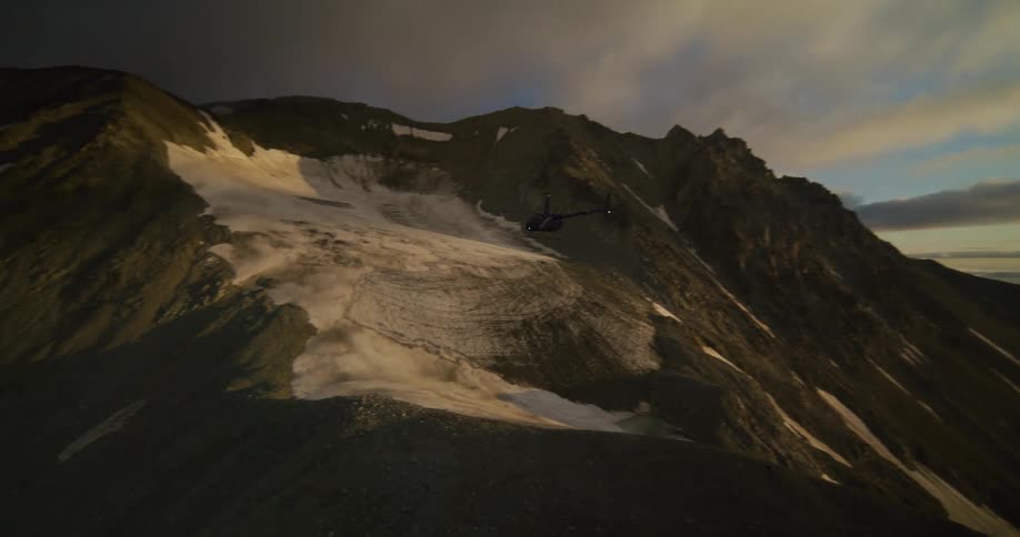 Epic aerial tracking shot of a helicopter flying through a vast mountain range and landing on a snowy peak at sunset