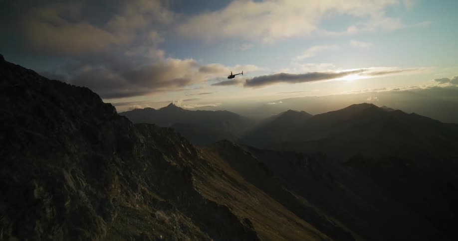 A helicopter is silhouetted against a breathtaking sunrise as it flies over a vast mountain range