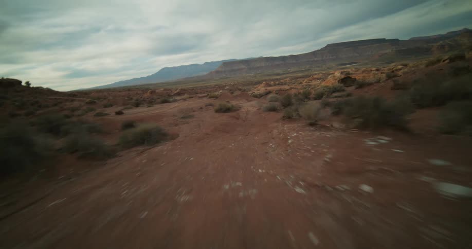 An exhilarating first-person drone flight soars over a rugged red dirt track in a vast desert landscape with mountains in the distance
