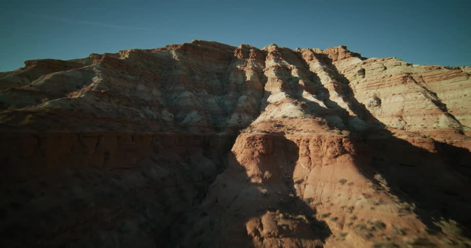Flying towards a majestic, layered red rock mountain formation under a clear blue desert sky