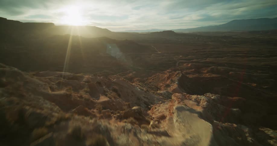 An epic aerial view flies alongside a rugged desert mountain before rising over the ridge to reveal the vast canyon landscape at sunset