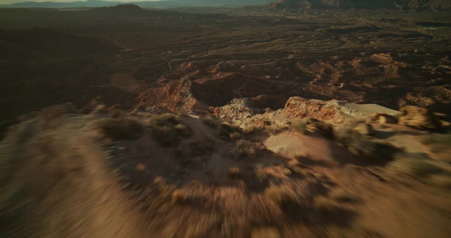 A thrilling first-person-view flight over a sun-drenched desert mountain, revealing a vast, rocky canyon landscape below