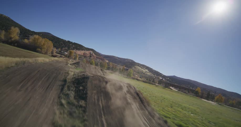 Slow-motion aerial view of motocross riders racing and jumping on a dirt track in the countryside