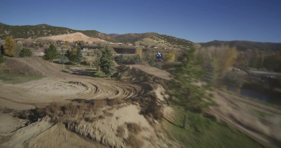 A slow-motion aerial shot follows a motocross rider as they race and jump along a winding dirt track