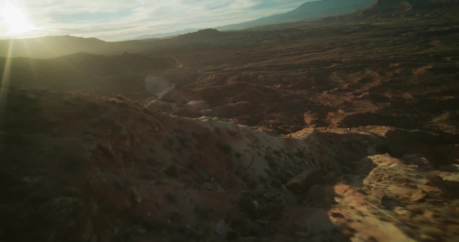 Dynamic FPV drone footage soars down a rugged desert mountain landscape at golden hour