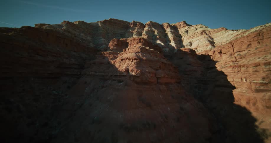 A fast-paced aerial ascent through a rugged desert canyon, revealing the majestic red rock formations against a clear blue sky