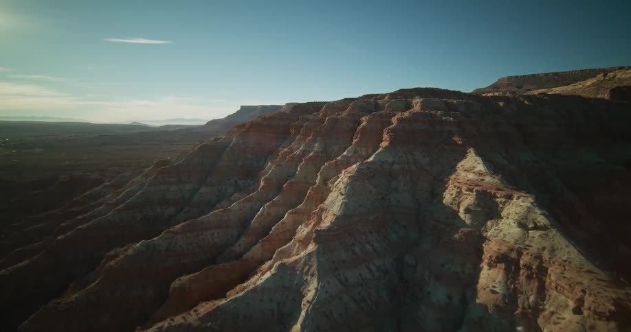 An epic aerial flight over the sun-drenched, layered ridges of red rock mountains in a vast desert landscape