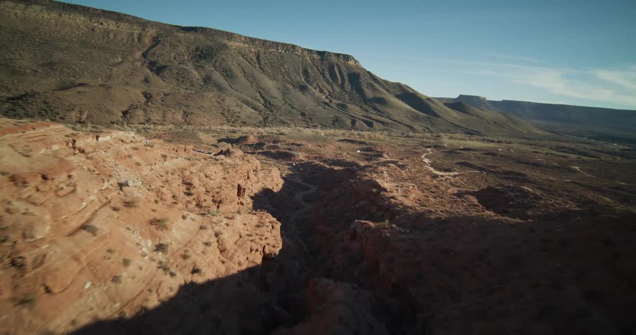 A stunning aerial view flies over the rugged red rock ridges and canyons of a vast desert landscape on a clear sunny day