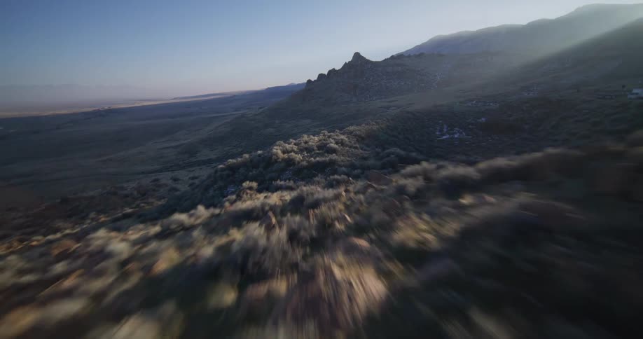 An exhilarating first-person view drone flight speeds low over a rocky mountain ridge at golden hour