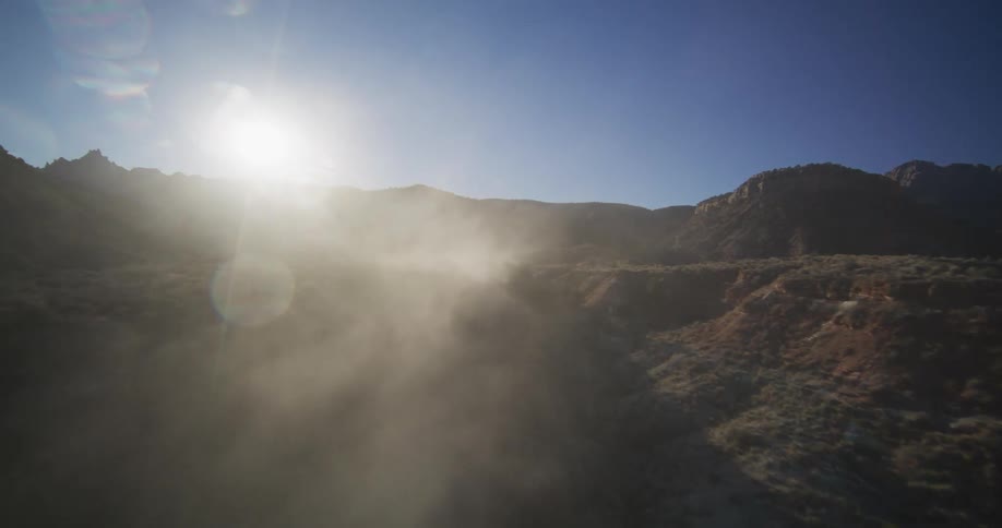 An epic aerial shot pushes through a dusty, sun-drenched canyon, revealing the rugged landscape