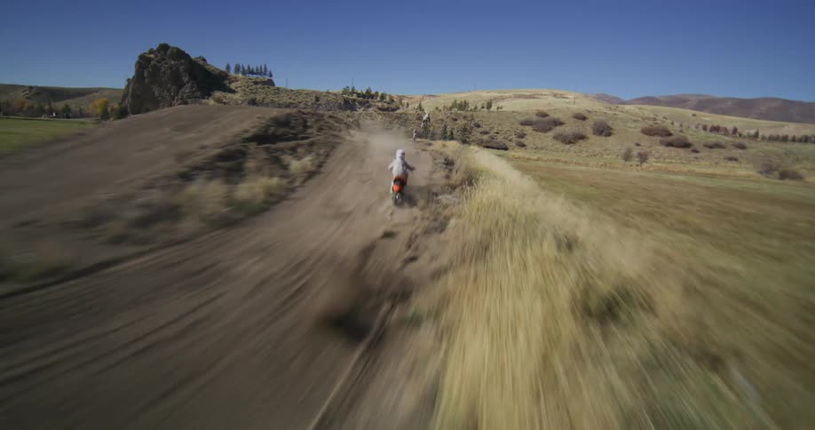 Dynamic follow-cam shot of a young motocross rider speeding and jumping on a rural dirt track under a clear blue sky