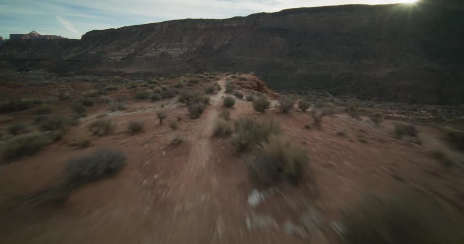 An exhilarating first-person-view drone flight speeds along a rugged desert ridgeline in a vast canyon landscape at sunset