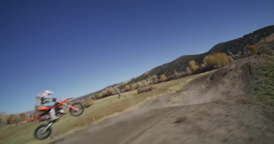 A dynamic first-person view follows a motocross rider racing and jumping along a dirt track through the countryside