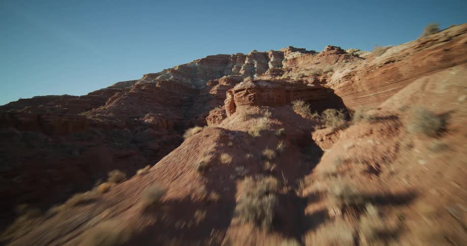 Dynamic FPV drone footage soars low through a rugged red rock desert canyon under a clear blue sky
