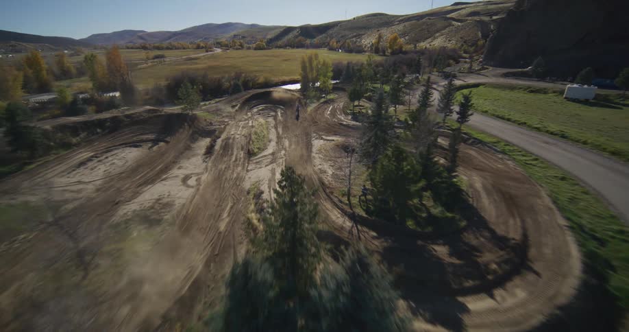 Thrilling FPV drone shot follows a motocross rider speeding down a dusty dirt track in the sunny countryside