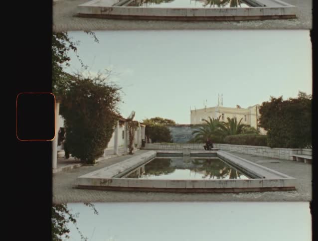 Vintage film shot of a tranquil courtyard with a large reflecting pool surrounded by lush greenery and historical architecture