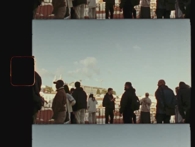 A crowd of people on a balcony overlook a European city in this vintage, split-frame film shot