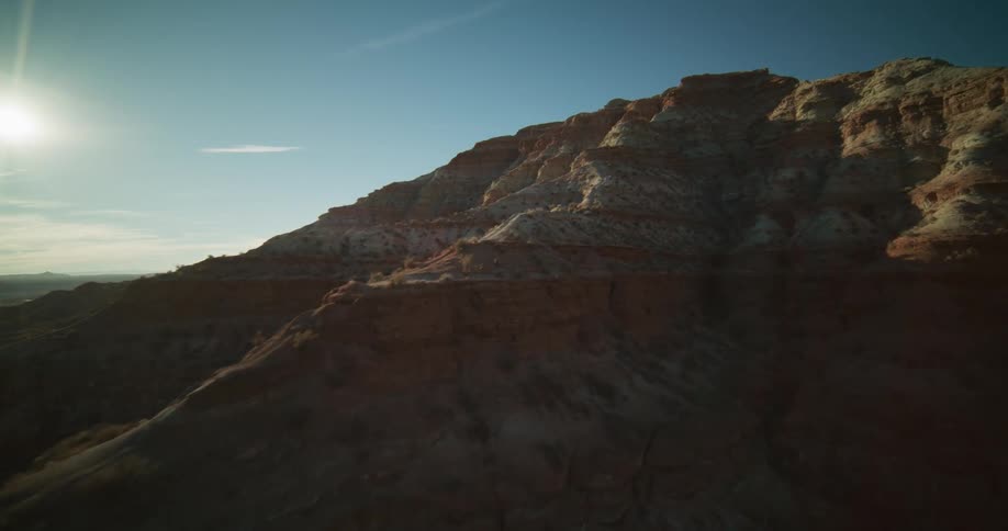 An immersive aerial view glides past the rugged, sun-kissed ridges of a vast desert mountain range