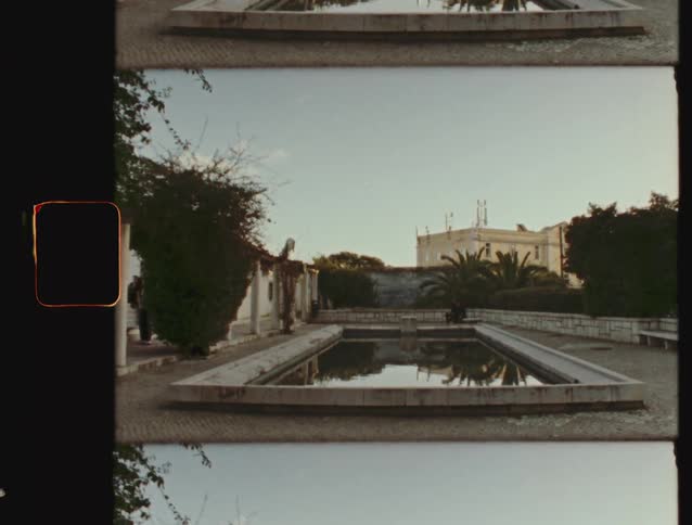 A vintage Super 8 film captures a quiet, sunlit formal garden with a large reflecting pool