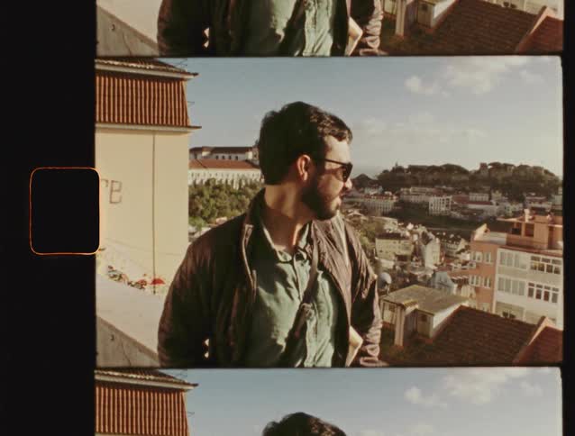 Vintage film strip footage of a smiling man in sunglasses waving from a viewpoint overlooking a sunny European city