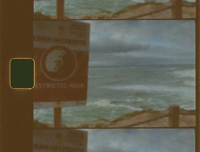 An ominous "Restricted Area" sign with a skull stands before a choppy sea on grainy, vintage Super 8 film