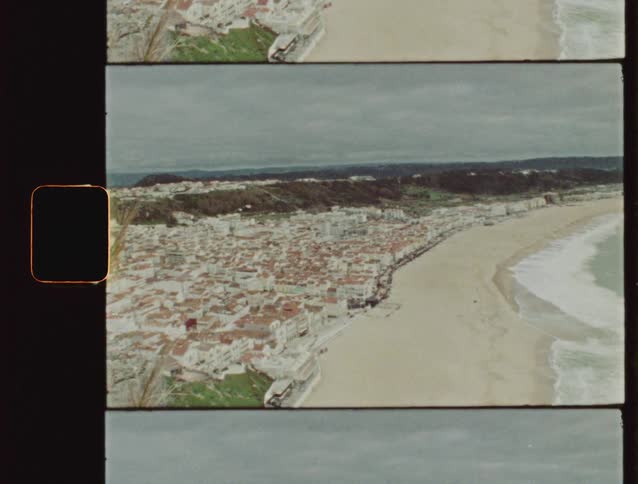 A vintage Super 8 film captures a high-angle panoramic view of the coastal town of Nazaré, Portugal, on an overcast day