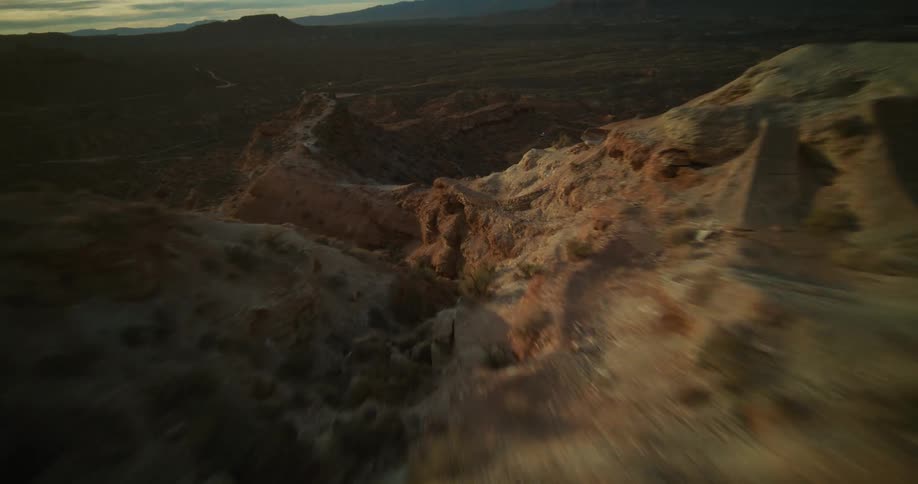 An exhilarating FPV drone flight soars along a rugged desert cliff face, revealing the golden sunrise over the vast canyon landscape