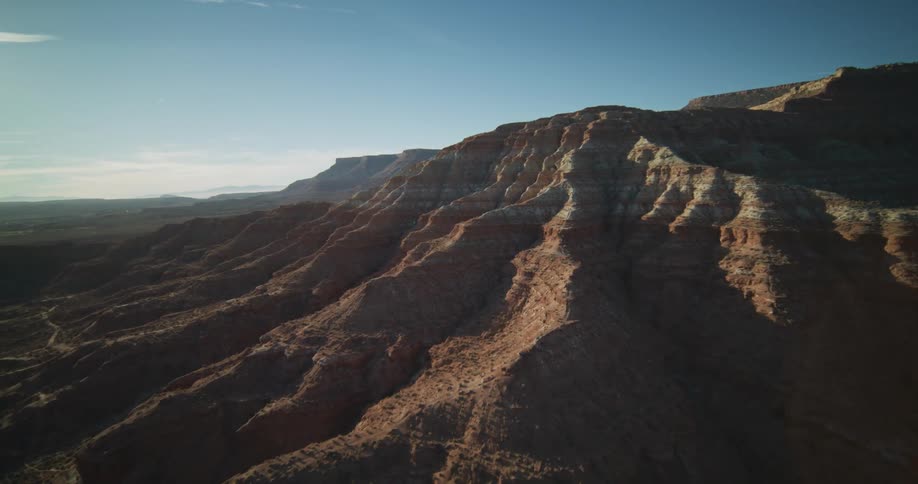 A majestic aerial pullback reveals a stunning desert canyon landscape under a clear, sunny sky